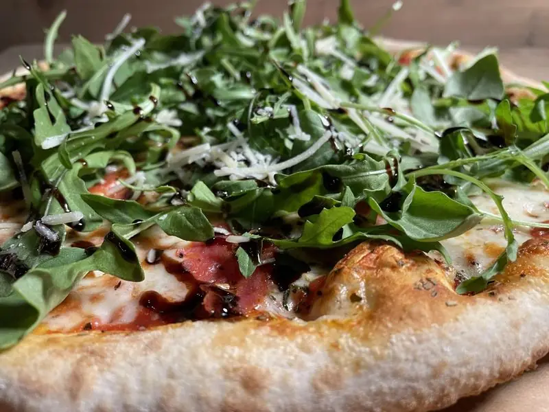 Macro shot of a salami, arugula, parmesan and balsamic pizza with a puffy, leopard-spotted crust edge