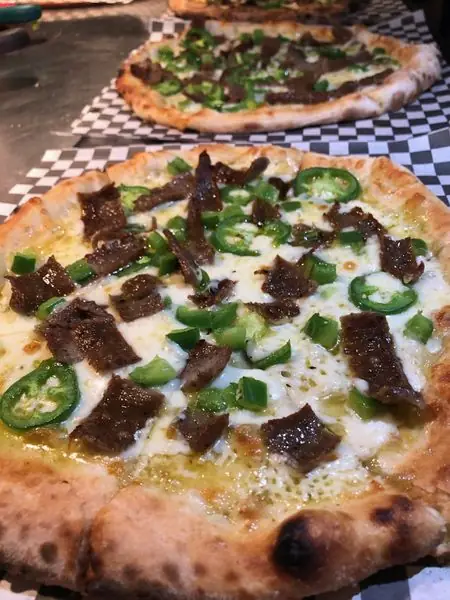 Two pizzas on a checkered cloth, one topped with steak and jalapeno